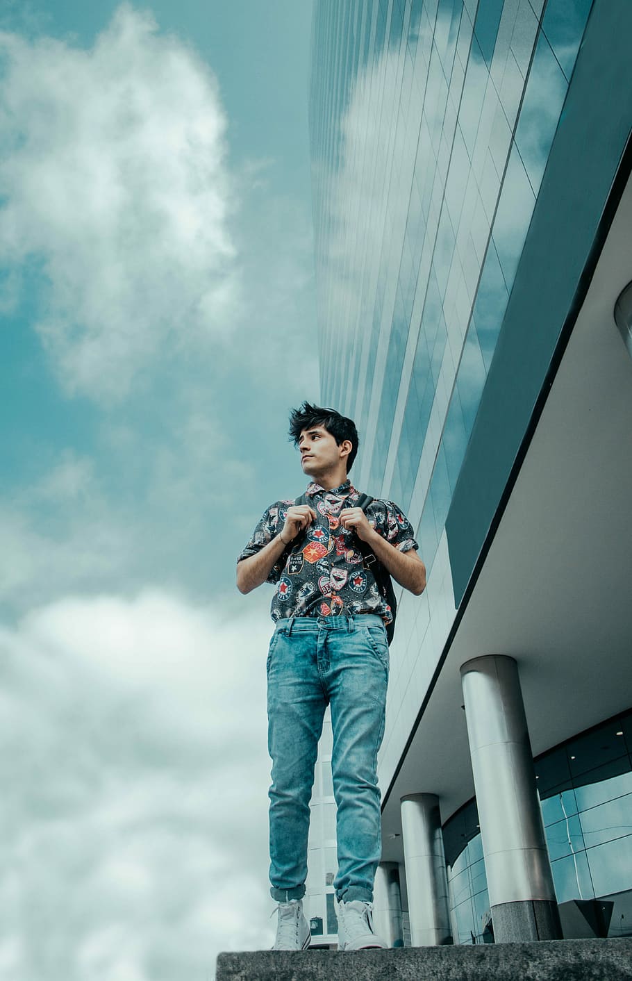man walking beside glass building under cloudy blue sky during daytime, man in blue denim pants standing on concrete floors looking on right, HD wallpaper