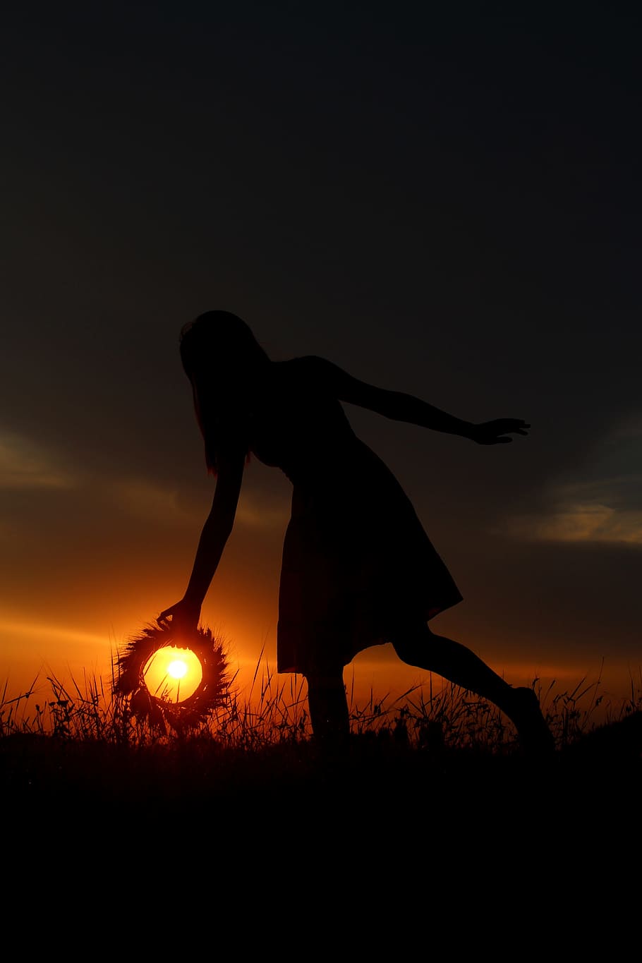 silhouette of woman holding wreath with sun in background during golden hour HD wallpaper