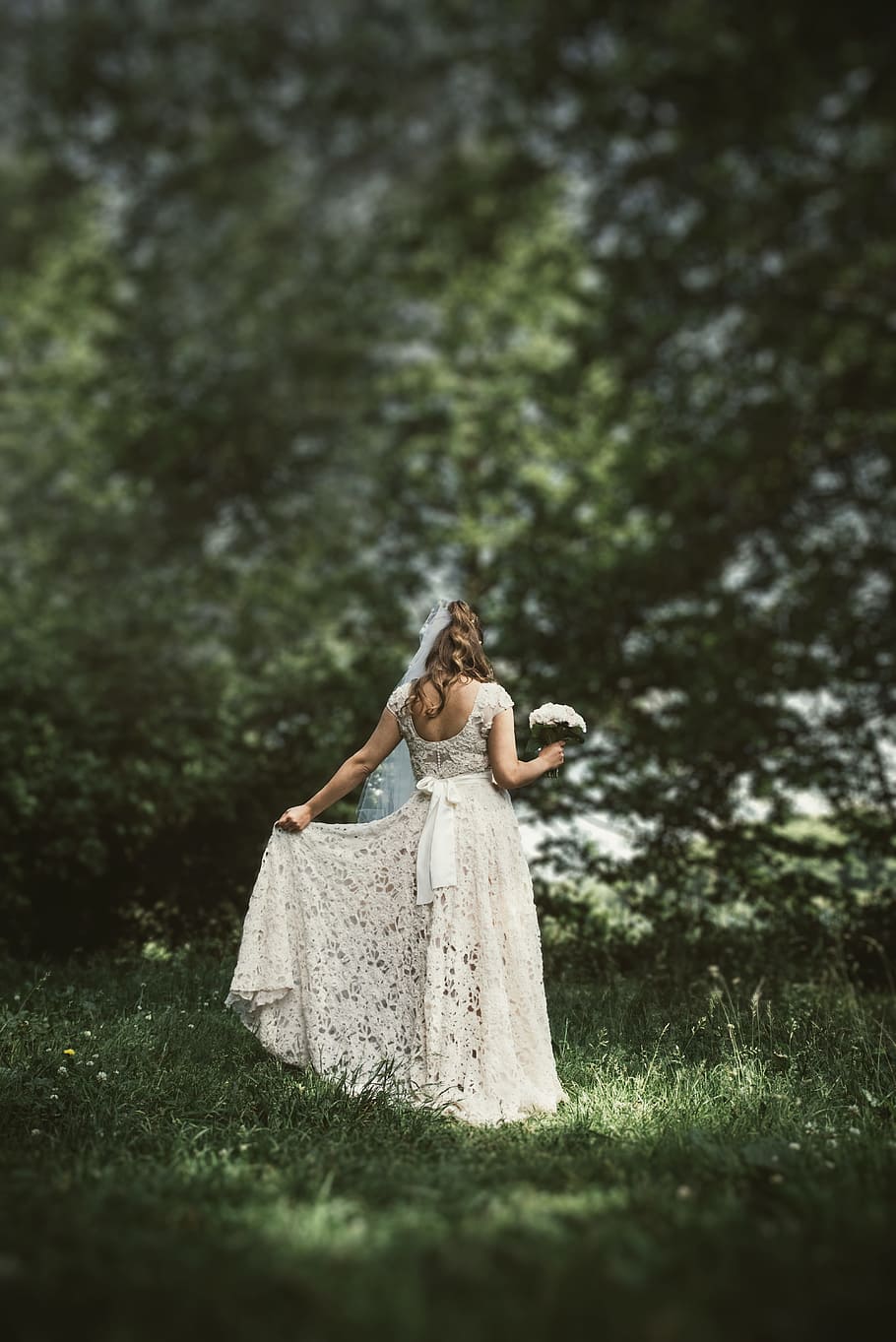 woman in white lace wedding dress holding a white bouquet surrounded with trees HD wallpaper