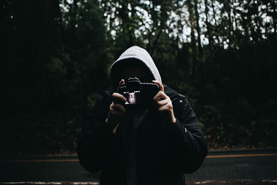 person holding camera, man in gray and black hooded jacket taking photo while standing near road