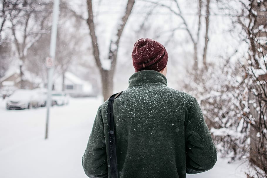 person in red knit cap and green top looking at trees with snow, man black green coat standing near trees covered by snow with vehicle ahead during winter HD wallpaper