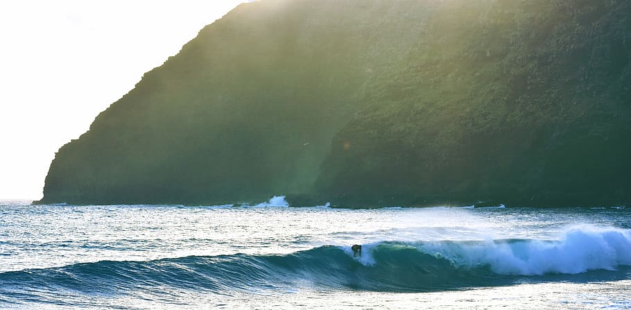 sea wave during daytime, person riding on surfboard near mountain HD wallpaper