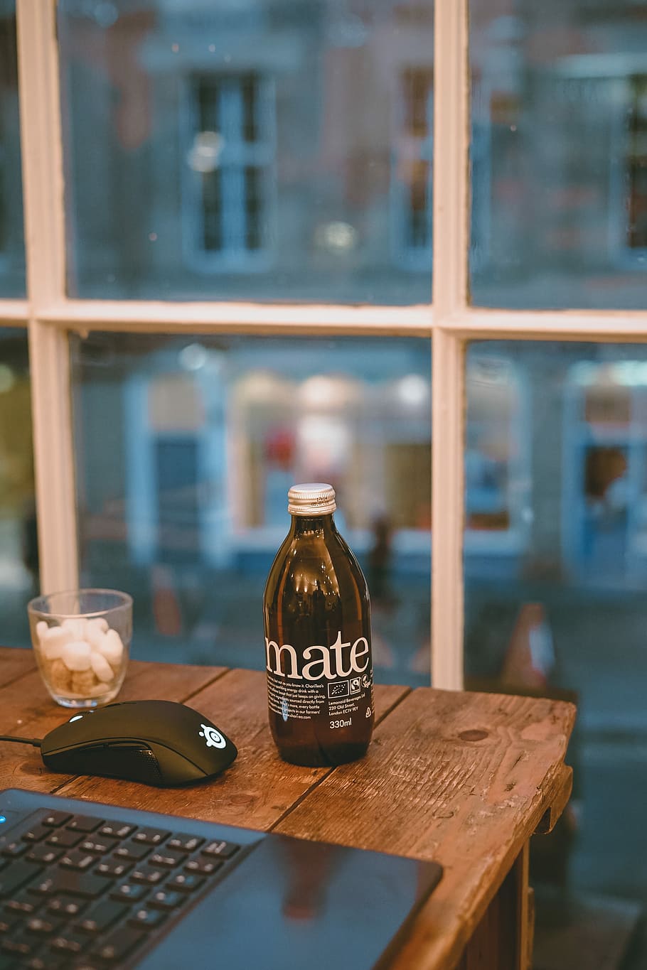 brown glass bottle near drinking glass and laptop on brown wooden table, mate labeled bottle on table beside Steelseries mouse HD wallpaper