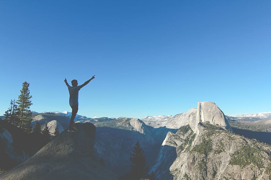 person standing on rock hands up, man raising hands while standing on hill during daytime