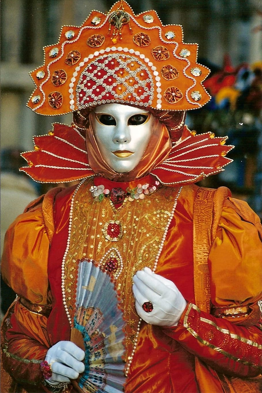 person in brown and orange traditional outfit holding fan, mask