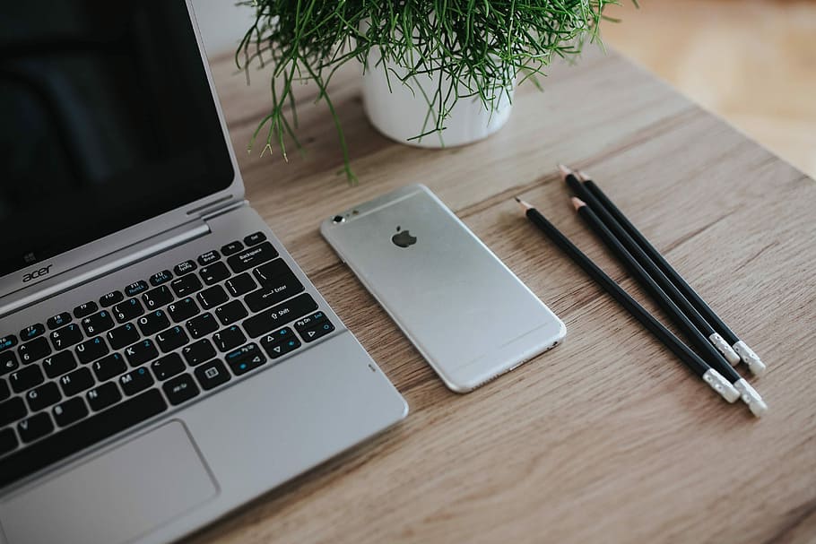 Silver Acer laptop on a wooden desk with a green plant, pencils and an Apple iPhone HD wallpaper