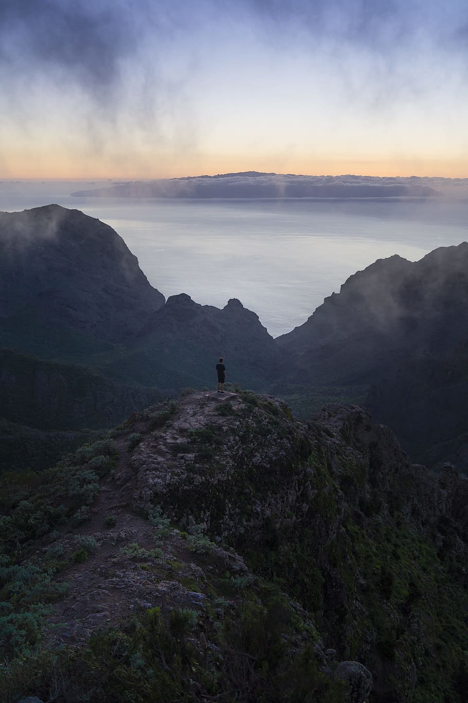 person standing on rock monolith, man standing on mountain cliff overlooking body of water under grey cloudy sky during daytime HD wallpaper