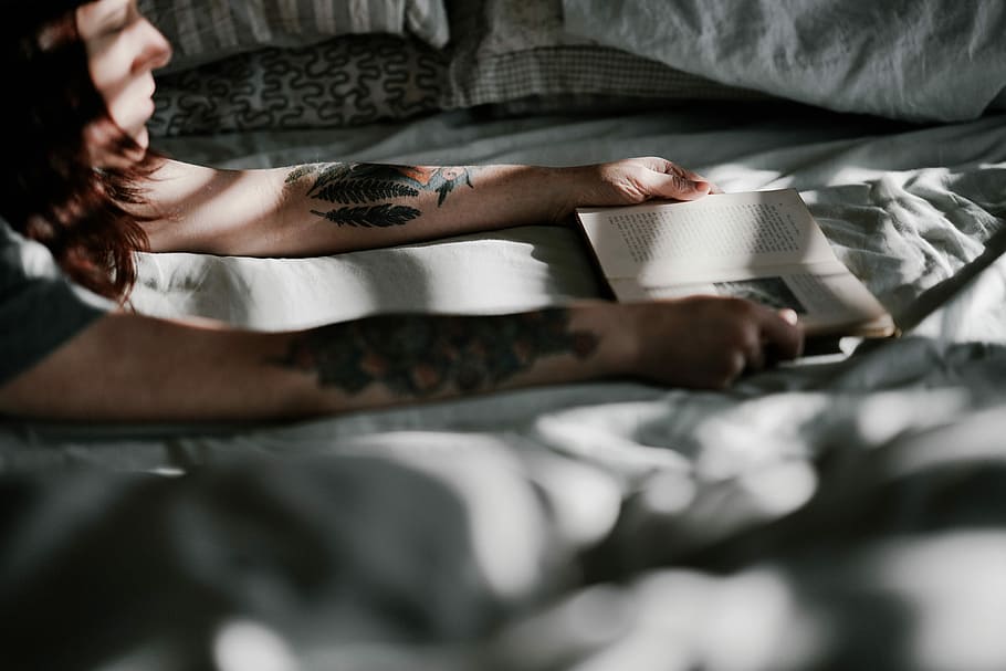 woman holding book while lying on bed, woman holding open book page on white textile HD wallpaper