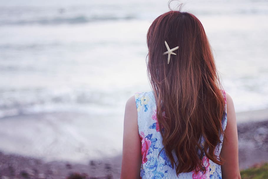 girl wearing white floral-pattern sleeveless shirt and starfish hairclip facing backwards near beach at daytime HD wallpaper