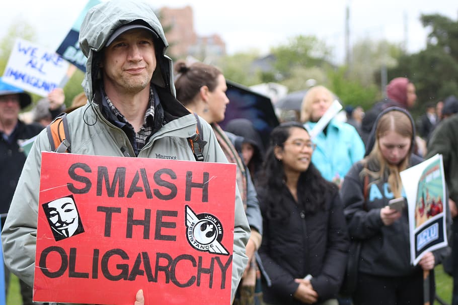 person holding smash the oligarchy sign outdoor during daytime