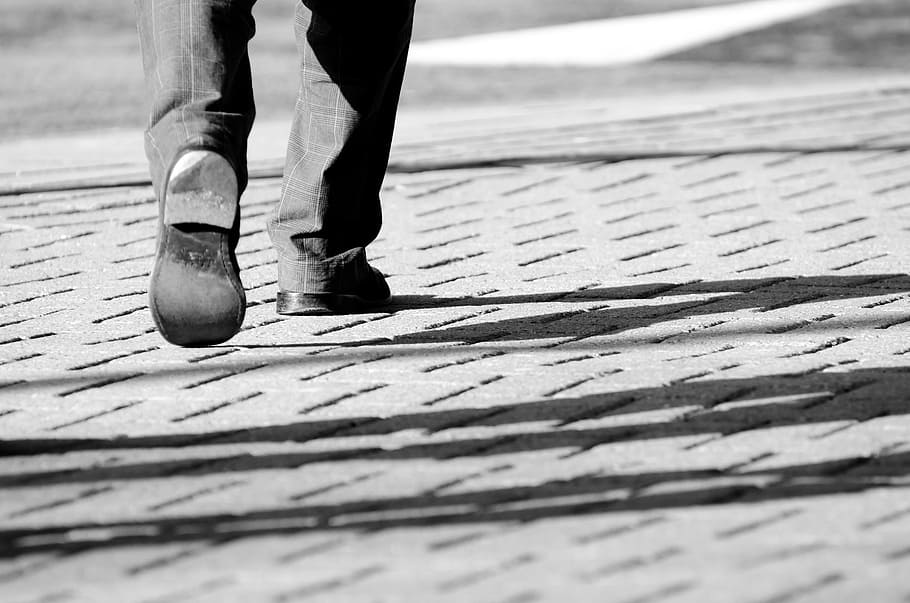 person wearing pair of black shoes while walking on gray pavement HD wallpaper