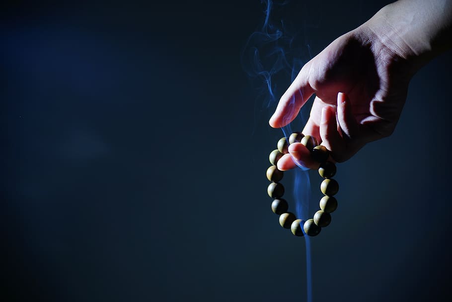 person holding beaded bracelet, hand, buddhist prayer beads, smoke