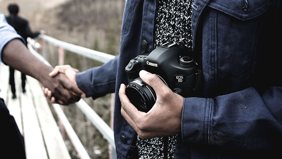 person shaking hands while holding Canon DSLR camera, holding hands HD wallpaper
