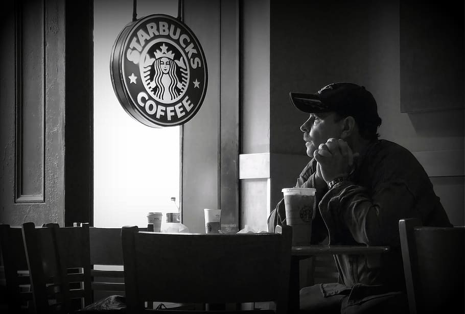 grayscale photo of man sitting at table near Starbucks poster, HD wallpaper