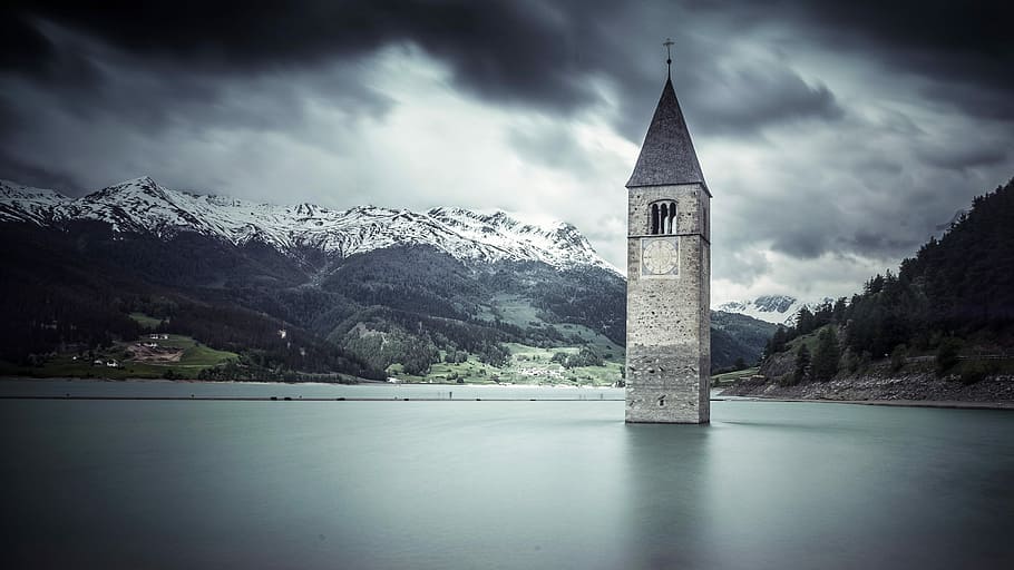 gray concrete building under cloudy sky, white concrete tower in body of water under gray clouds HD wallpaper