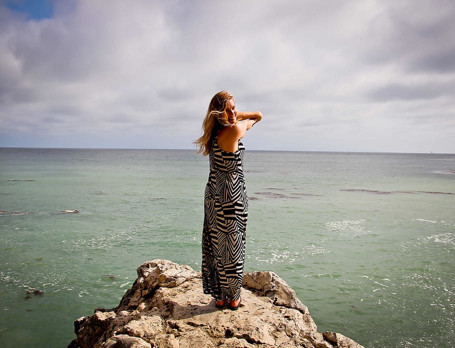 woman in black and white maxi dress on cliff near a sea during daytime