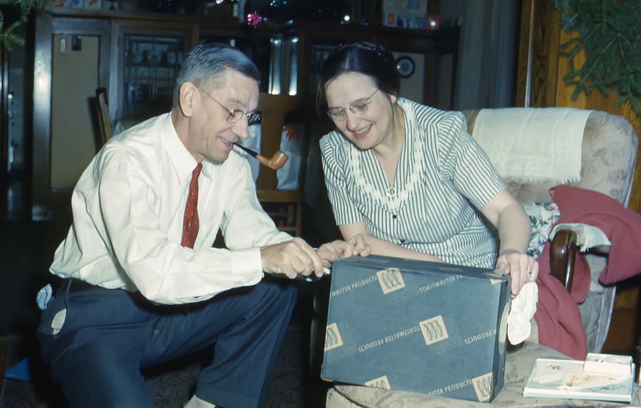 smiling woman sitting on chair holding box with man helping her HD wallpaper