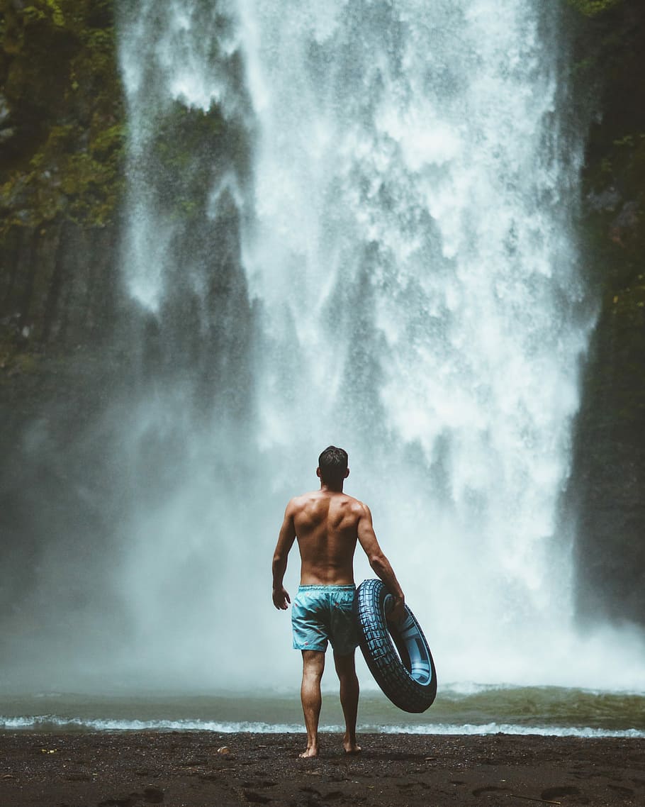 man holding swim ring walking towards waterfalls, motion, outdoors