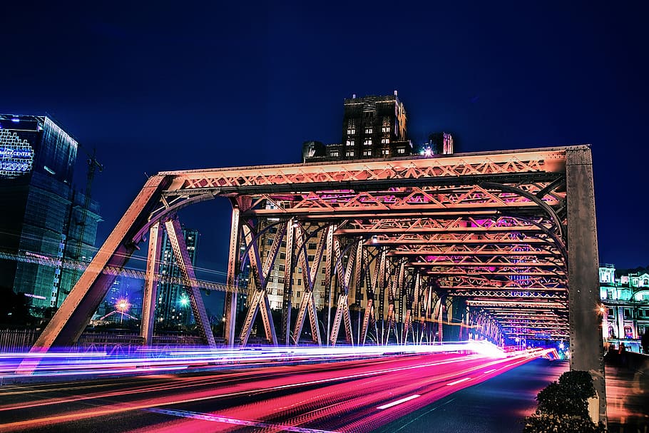 time lapse and light streaks photo of vehicle on bridge with high rise buildings in distant, brown suspension bridge in time lapse photography during night HD wallpaper