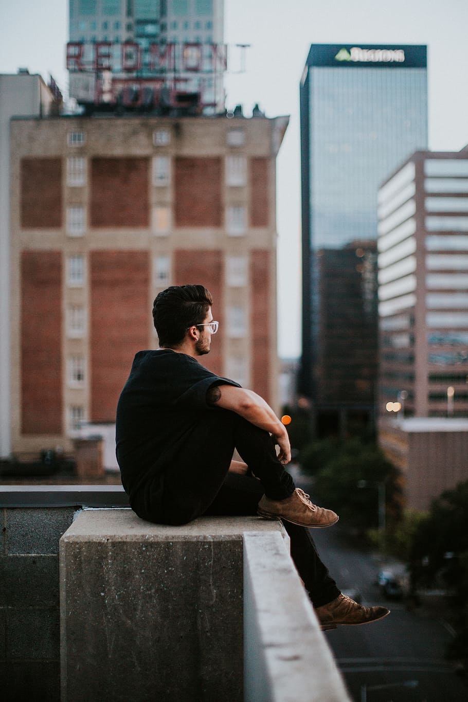 man sitting on white concrete building during daytime, man in black crew-neck shirt and black pants sitting on edge of a high surface during daytime, HD wallpaper