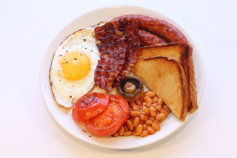 fried sunny side-up egg, sliced tomatoes, toast bread, sausage, ham and beans on white ceramic plate