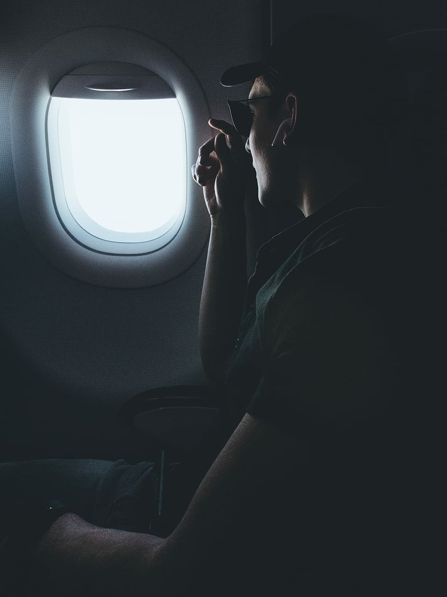 man inside airplane sitting on chair, person wearing wireless earphones looking outside airplane window