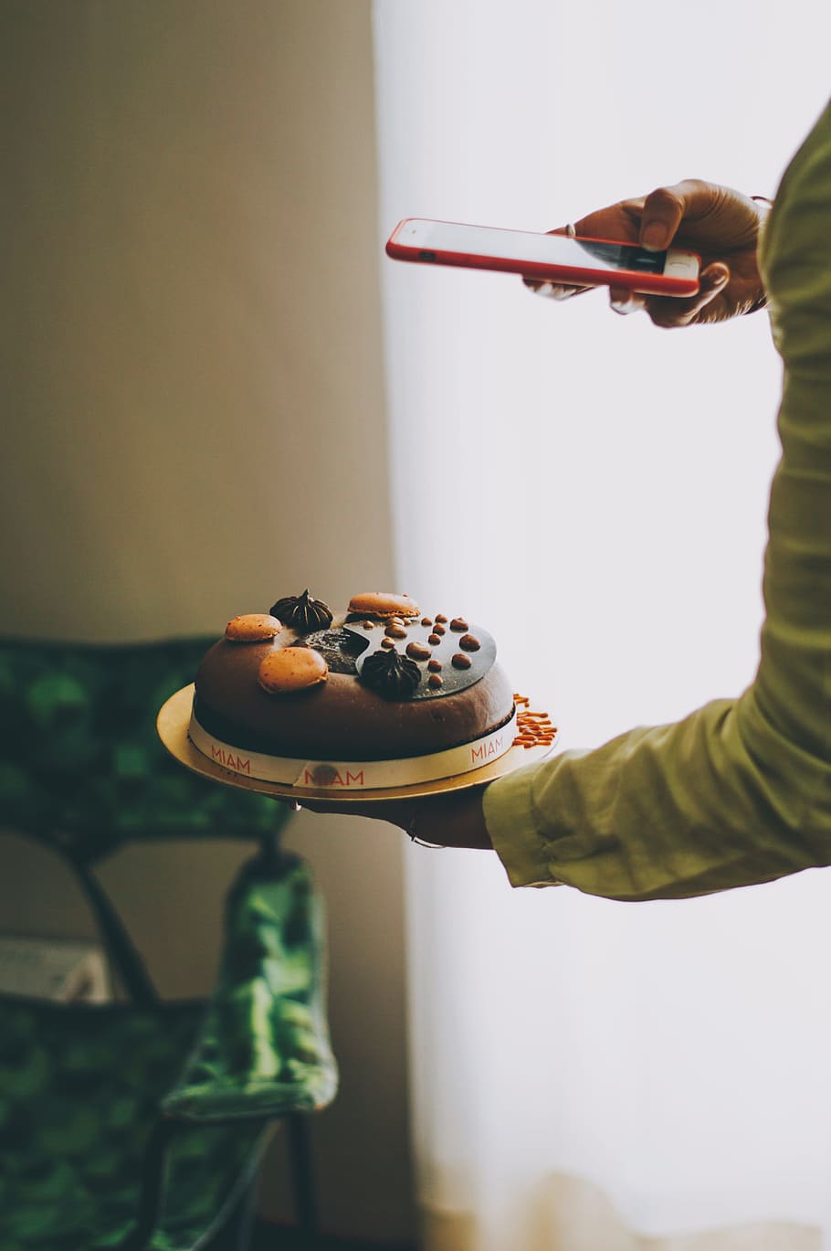 person holding iPhone taking photo of cake near curtains, person holding round white and brown icing-covered cake using iPhone HD wallpaper