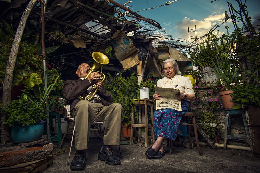 Clasic, man playing wind instrument near woman reading newspaper