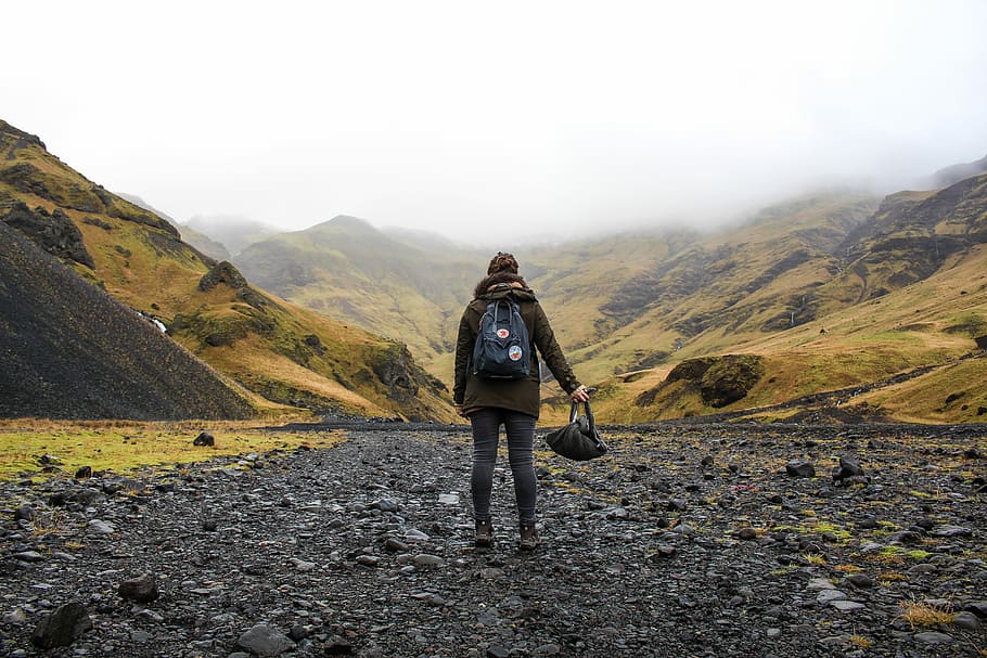 person holding bag standing on valley during daytime, person standing in the middle of the mountain foot HD wallpaper