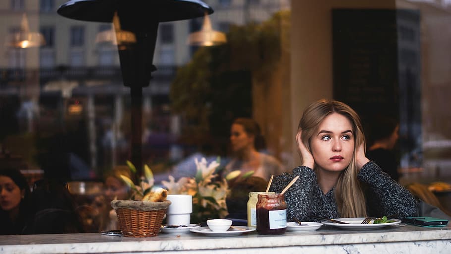 woman in grey sweater sitting in front of marble table covering her ears HD wallpaper
