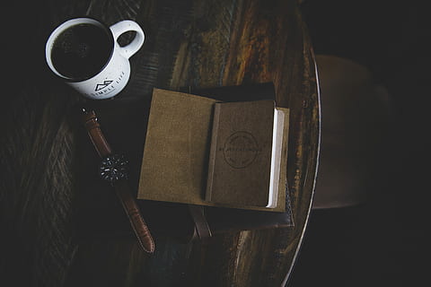 brown book near white ceramic mug and round black analog watch placed on brown wooden table HD wallpaper