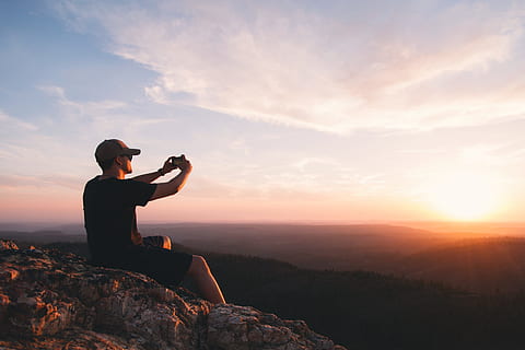 man sitting on mountain cliff taking picture, photography of man taking photo of sun HD wallpaper