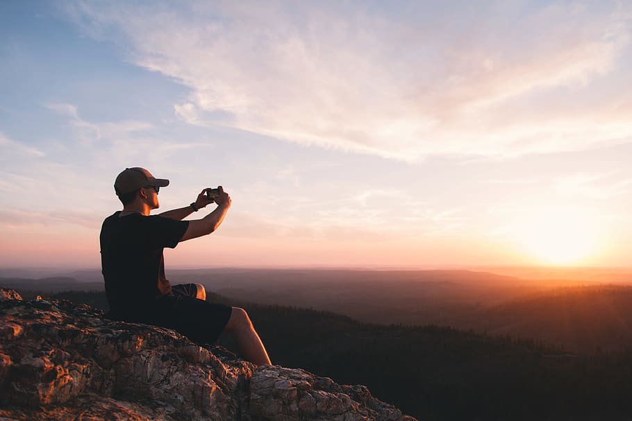man sitting on mountain cliff taking picture, photography of man taking photo of sun HD wallpaper