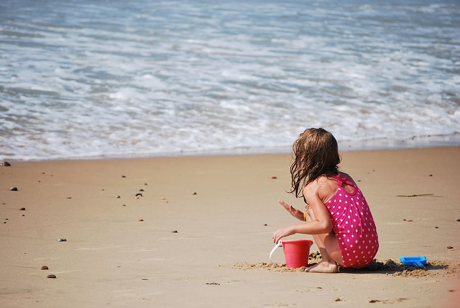 girl in pink and white polka-dot sleeveless onepiece playing on shoreline beside sea HD wallpaper
