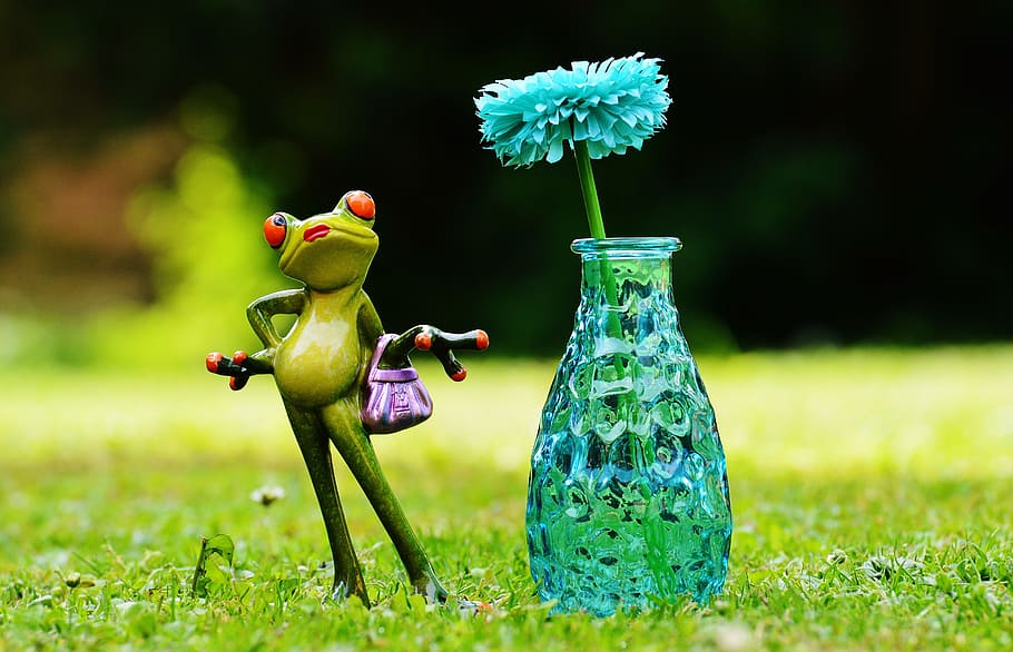 green frog carrying handbag near blue cut glass vase, flower