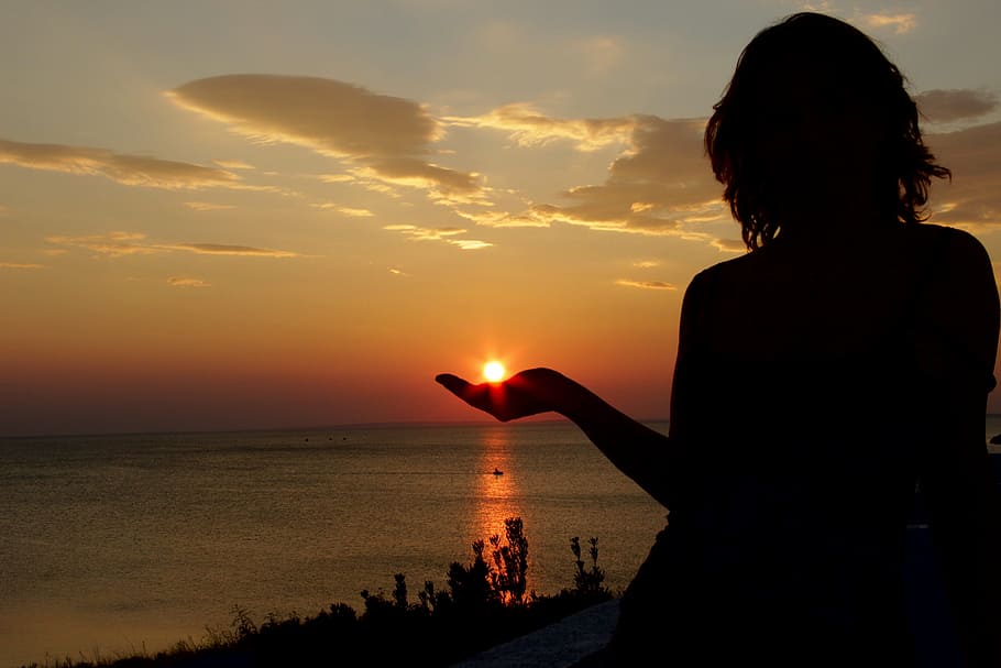 silhouette of forced perspective photography of woman facing sunset while sun on left hand HD wallpaper