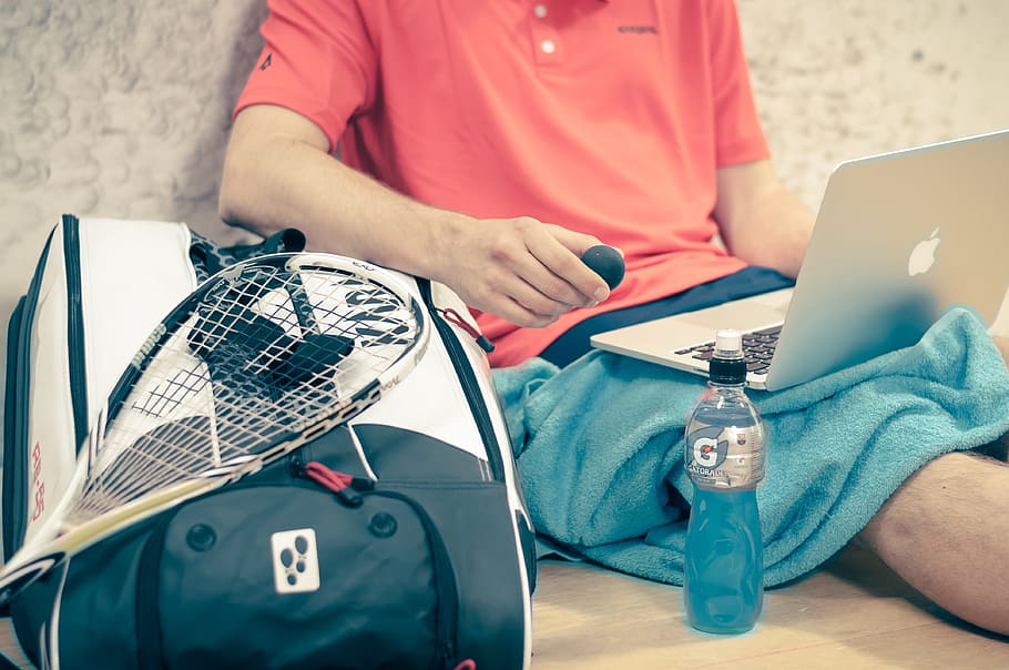 man sitting on beige floor facing opened MacBook near tennis gear, HD wallpaper