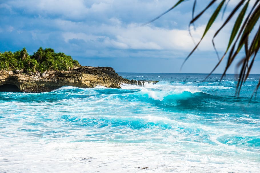 ocean waves rushing trough stones, island surrounded by water under cloudy sky during daytime HD wallpaper