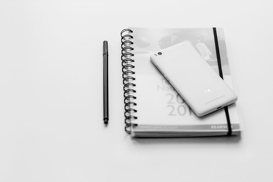 white Android smartphone on gray spiral book near black pen, notebook