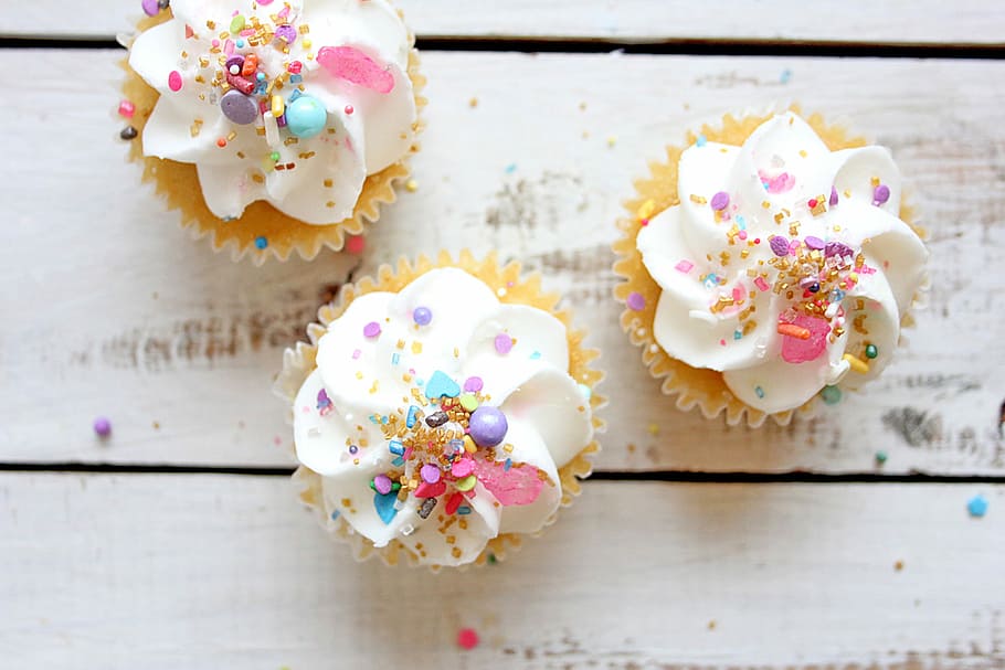 Cupcakes with sprinkles on wooden background, three white icing covered cupcakes HD wallpaper