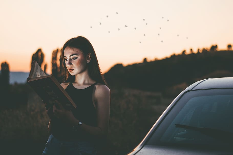 photo of a woman reading book while leaning on car during daytimne HD wallpaper