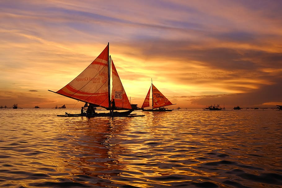 silhouette of sail boats floating on body of water, two brown and red sailing boats during sunset
