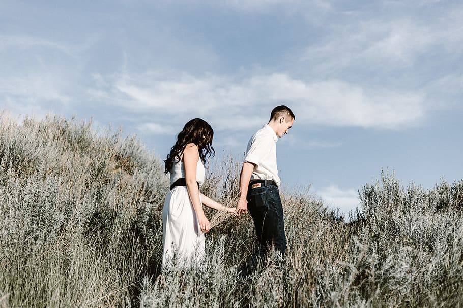 couple walks of grassy field, man and woman holding hands while walking on grass field at day time HD wallpaper