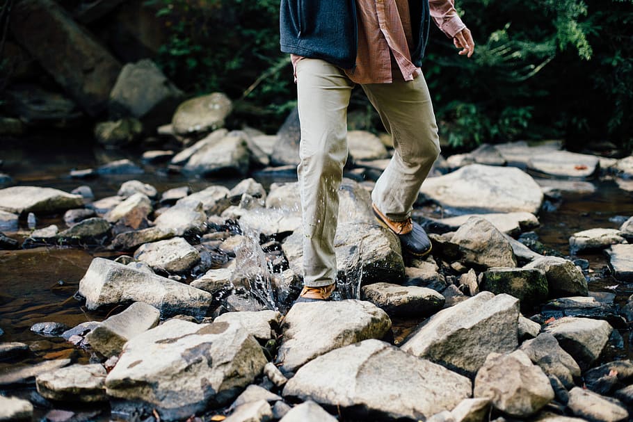 person on brown denim jeans walking on rocky river at daytime HD wallpaper