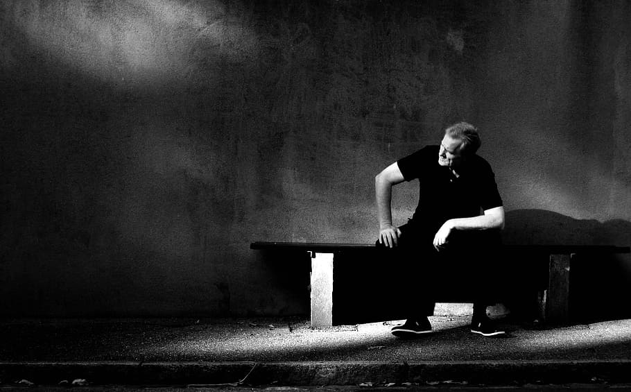 man wearing black shirt and black pants sitting on bench near wall HD wallpaper