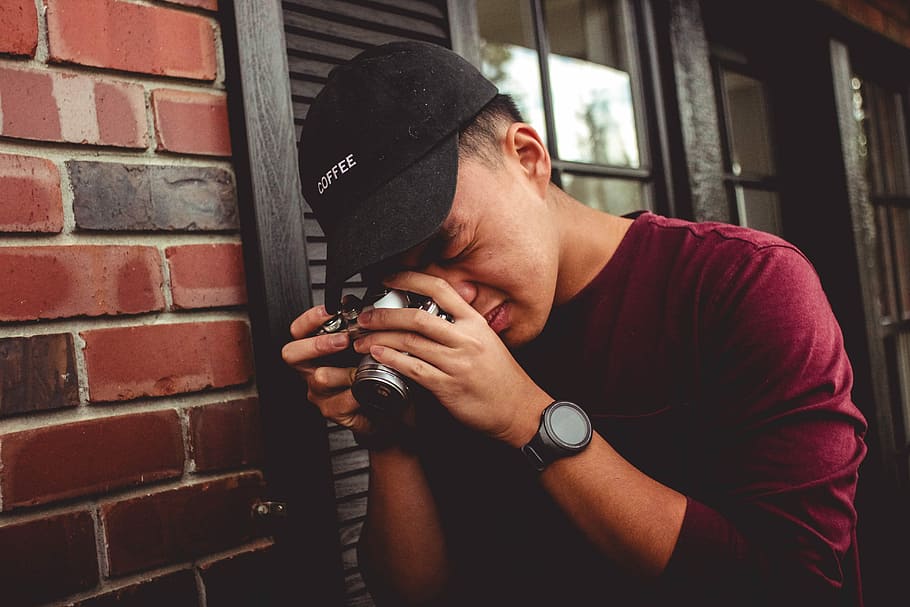 man leaning on wall holding camera near window, man holding camera near wall while taking photo HD wallpaper