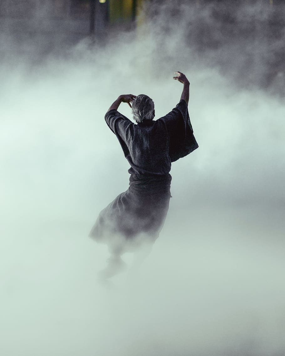 man in black robe surrounded by smoke inside room, man dancing surrounded by smoke