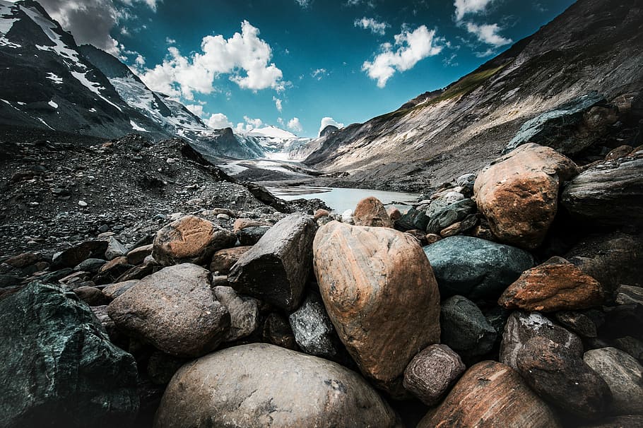 stone at the mountain near body of water, brown and gray stones near mountain under blue sky at daytime HD wallpaper