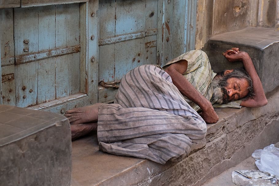 man sleeping beside closed door, india, misery, poverty, road