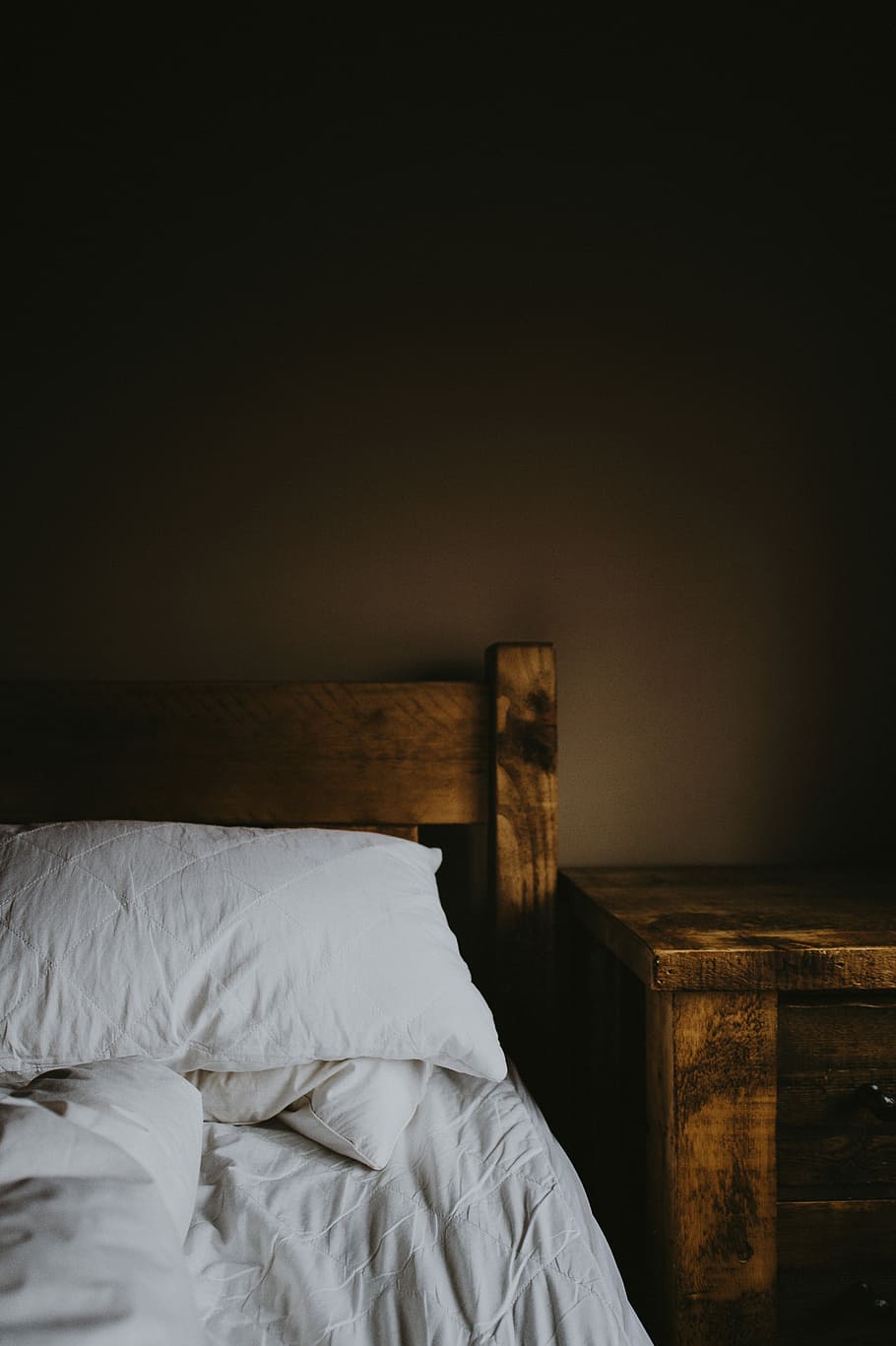 Bedtime, brown wooden nightstand beside bed with white sheet